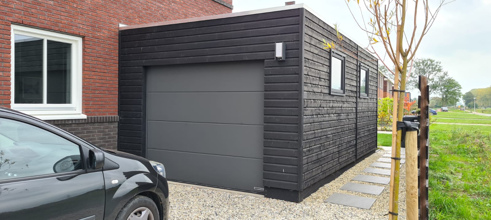 Houten garage in het zwart met een auto ervoor